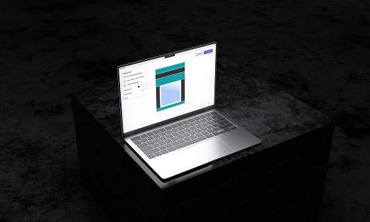 Open laptop on a dark surface displaying a design or layout editing interface on screen.