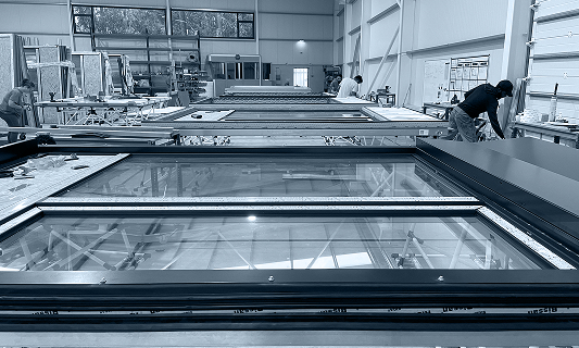 Workers assembling large window frames in a spacious industrial workshop.