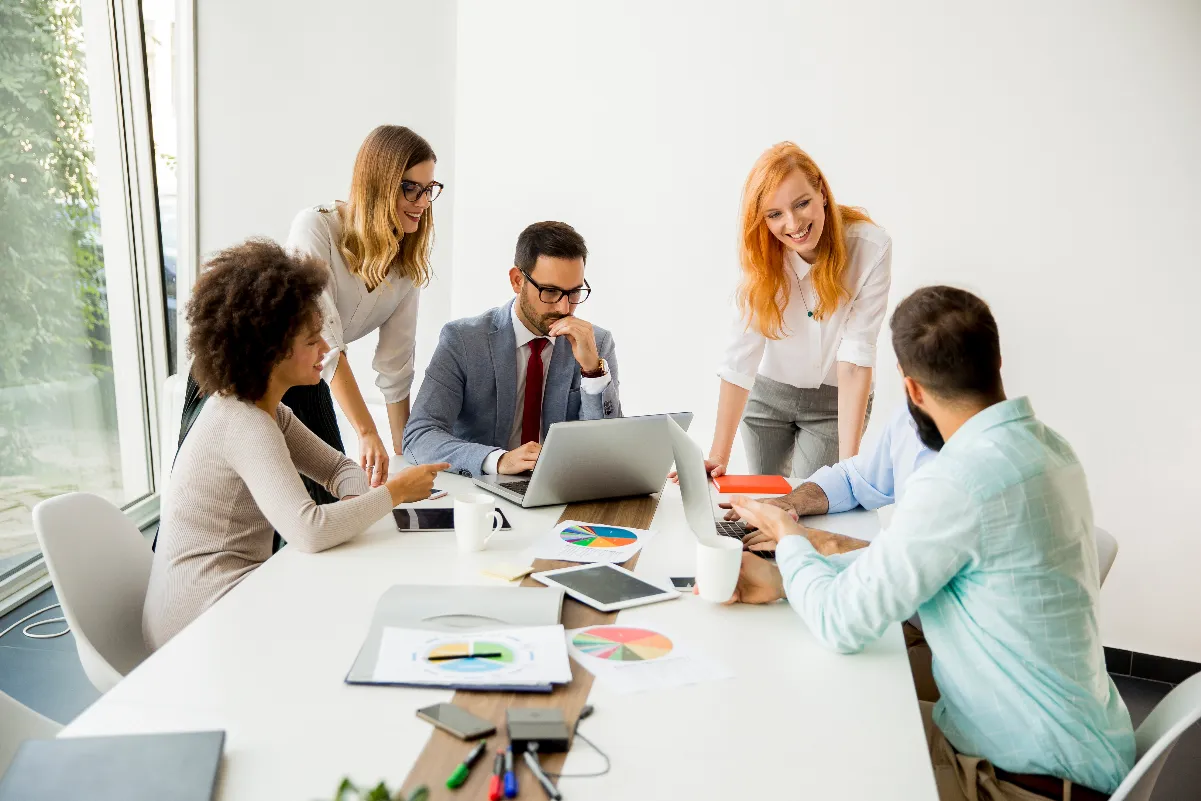 Team members collaborating around a table with a laptop