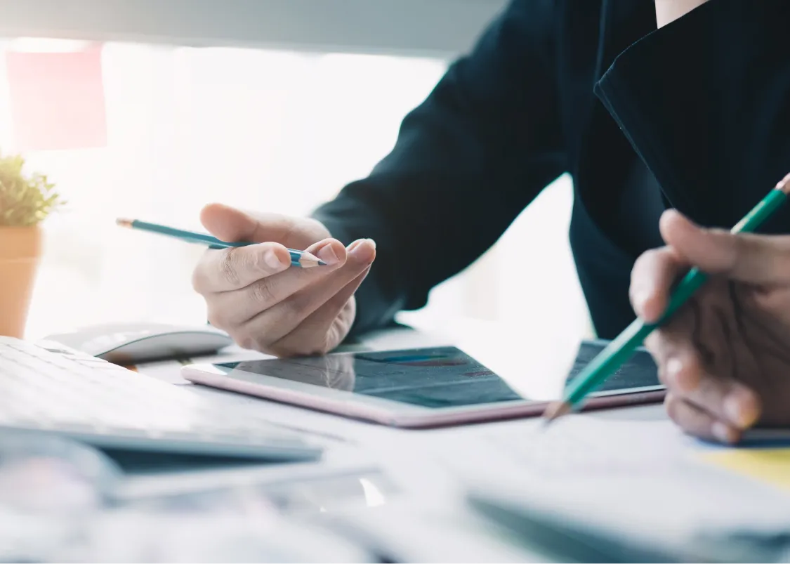 Hands holding pencils over a tablet and documents at a desk