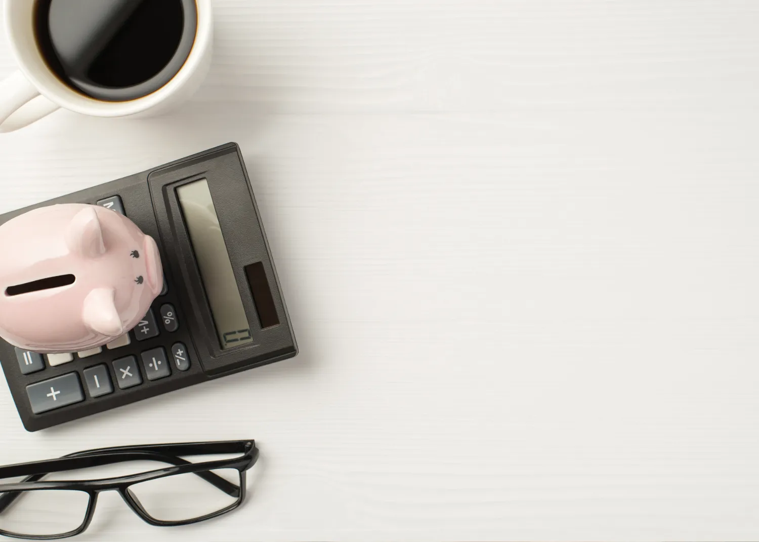 Piggy bank on a calculator beside a cup of coffee