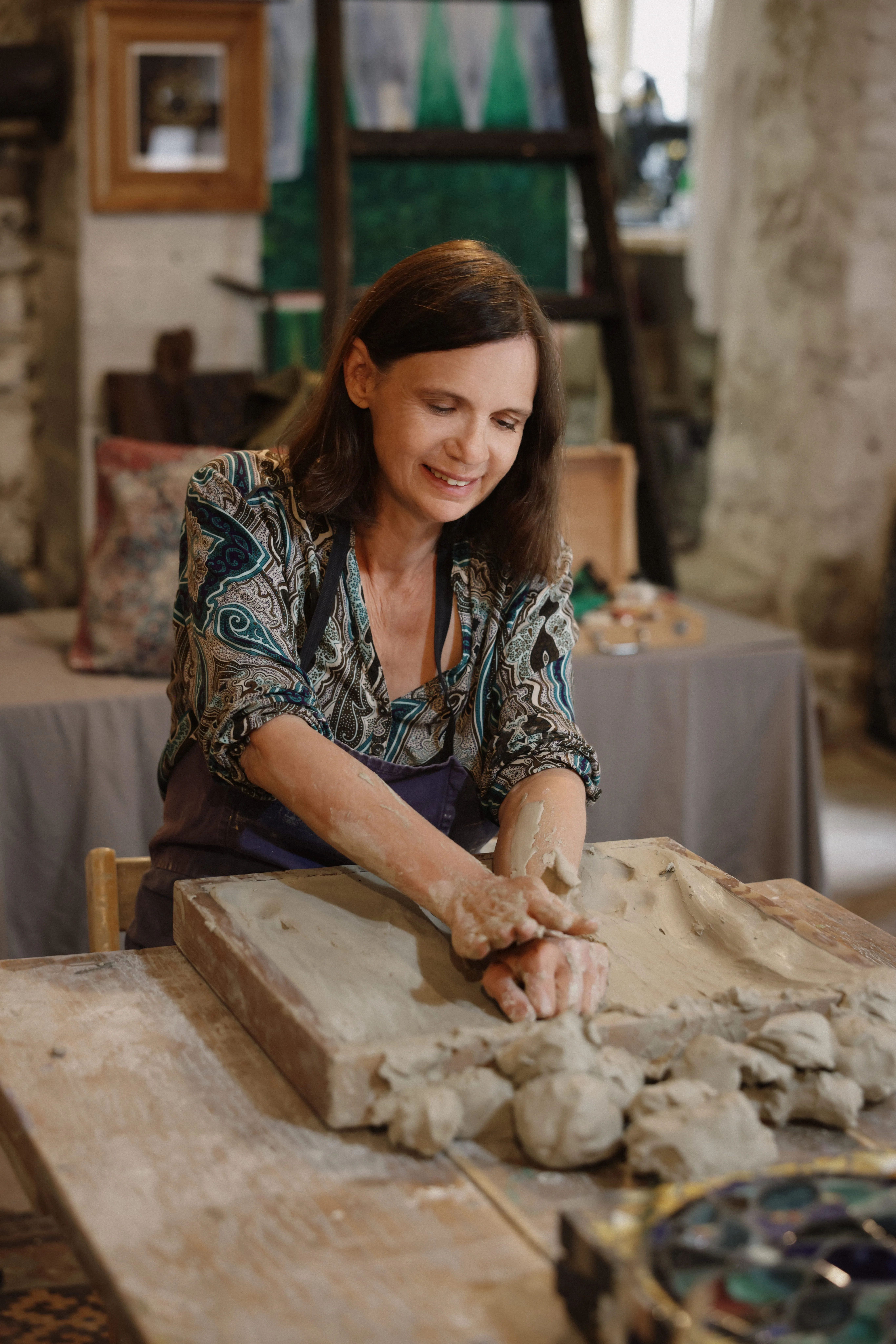 Woman shaping clay with her hands at a pottery workshop table.
