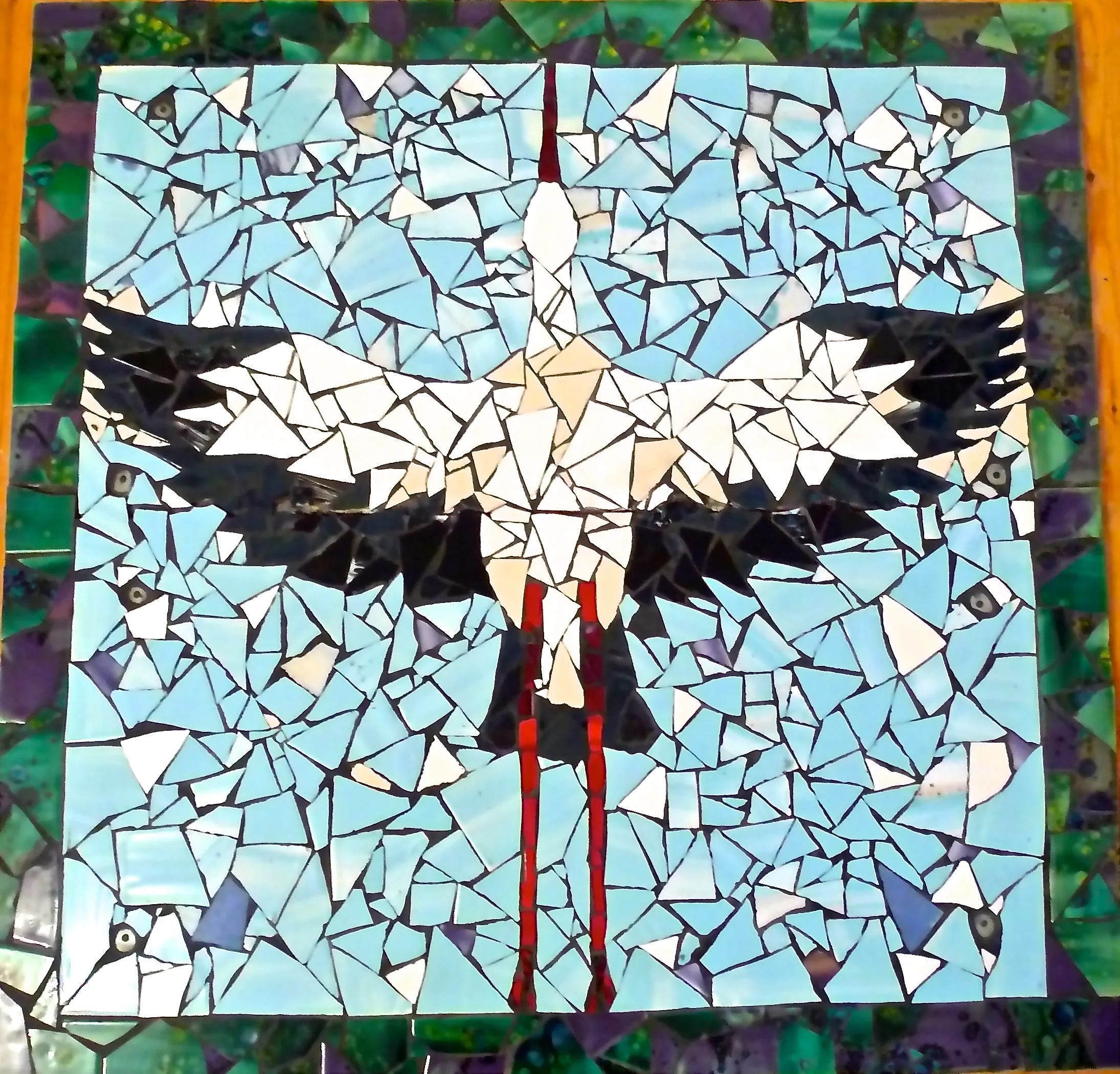 Mosaic artwork of a large bird with outstretched wings and long red legs set against a background of blue and green tiles.