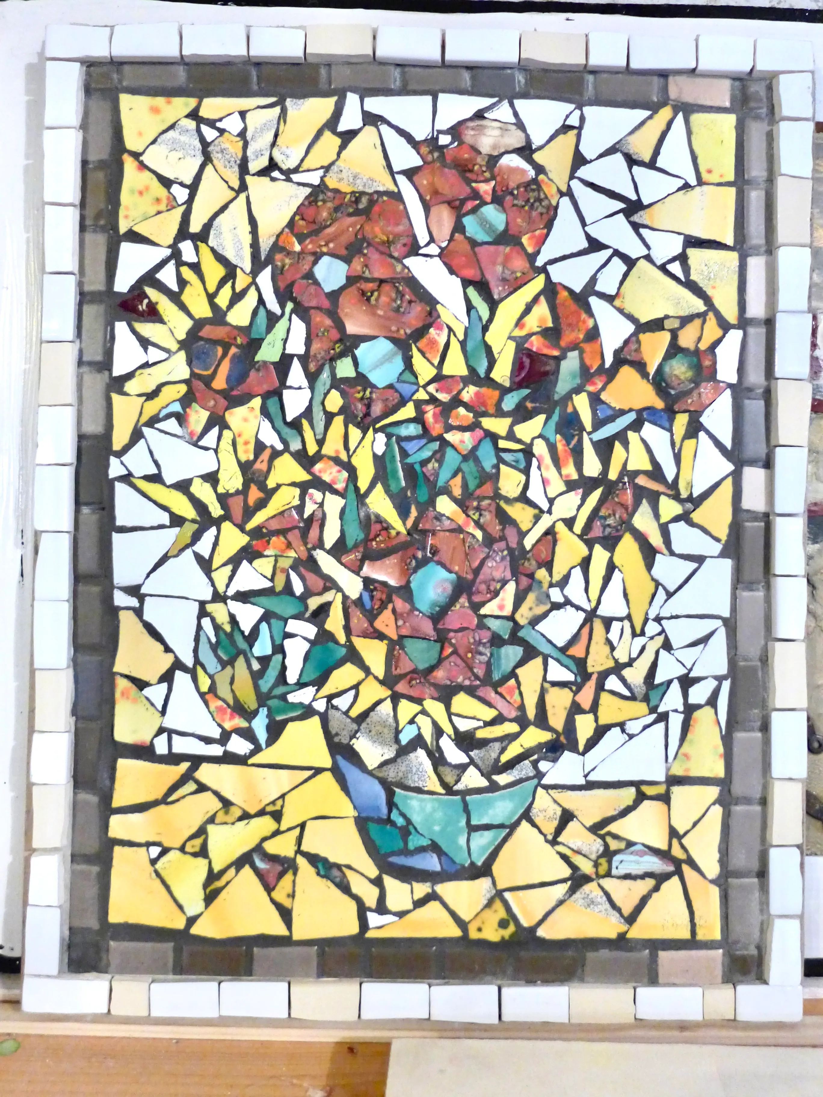 Colorful mosaic artwork of a flower bouquet in a vase made from irregular pieces of ceramic and glass tiles.