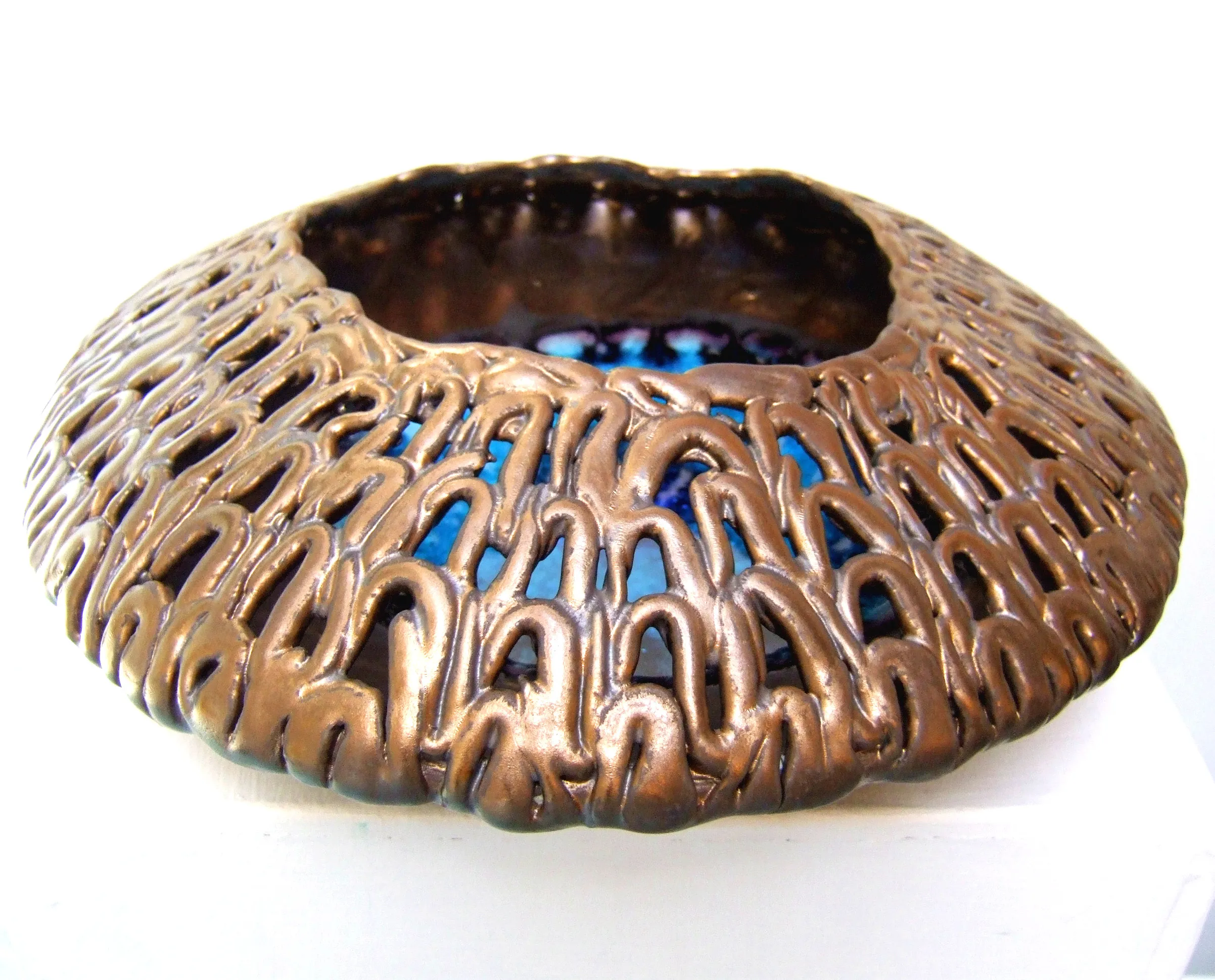 Bronze-colored ceramic vessel with an openwork organic pattern and a blue interior, placed on a white surface.