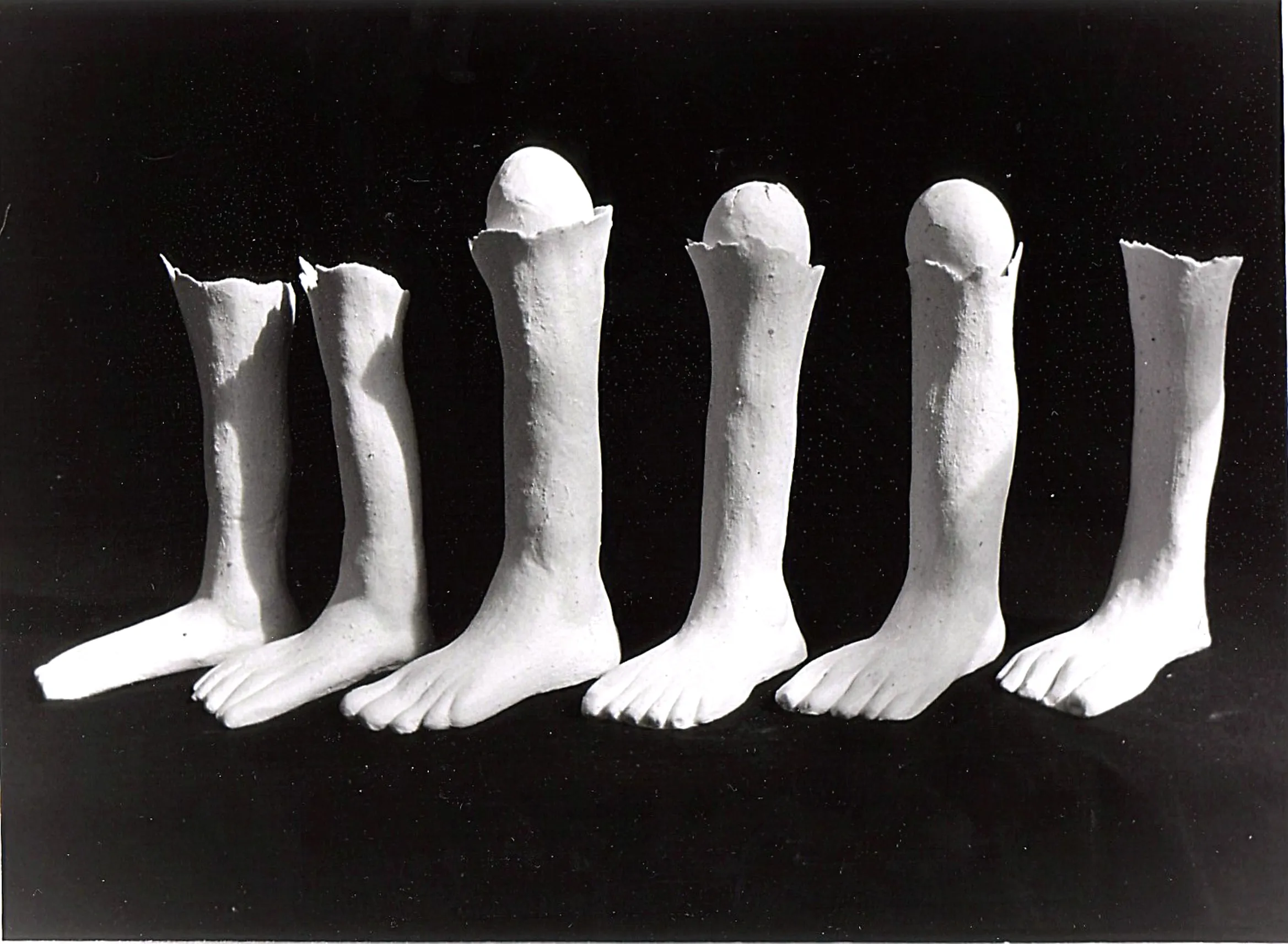 Black and white photo of six plaster feet sculptures, three containing whole eggs inside the hollow tops.