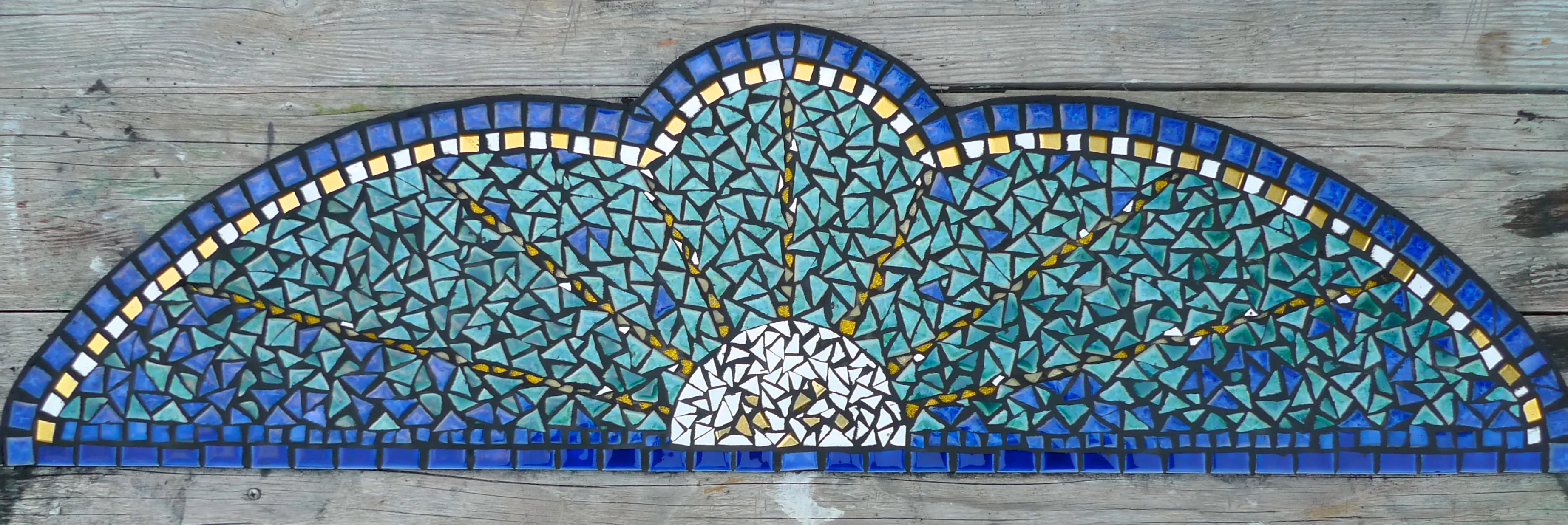 Mosaik in Halbkreisform mit blau-grünen und weißen Glasstücken, die eine stilisierte Sonne darstellen.