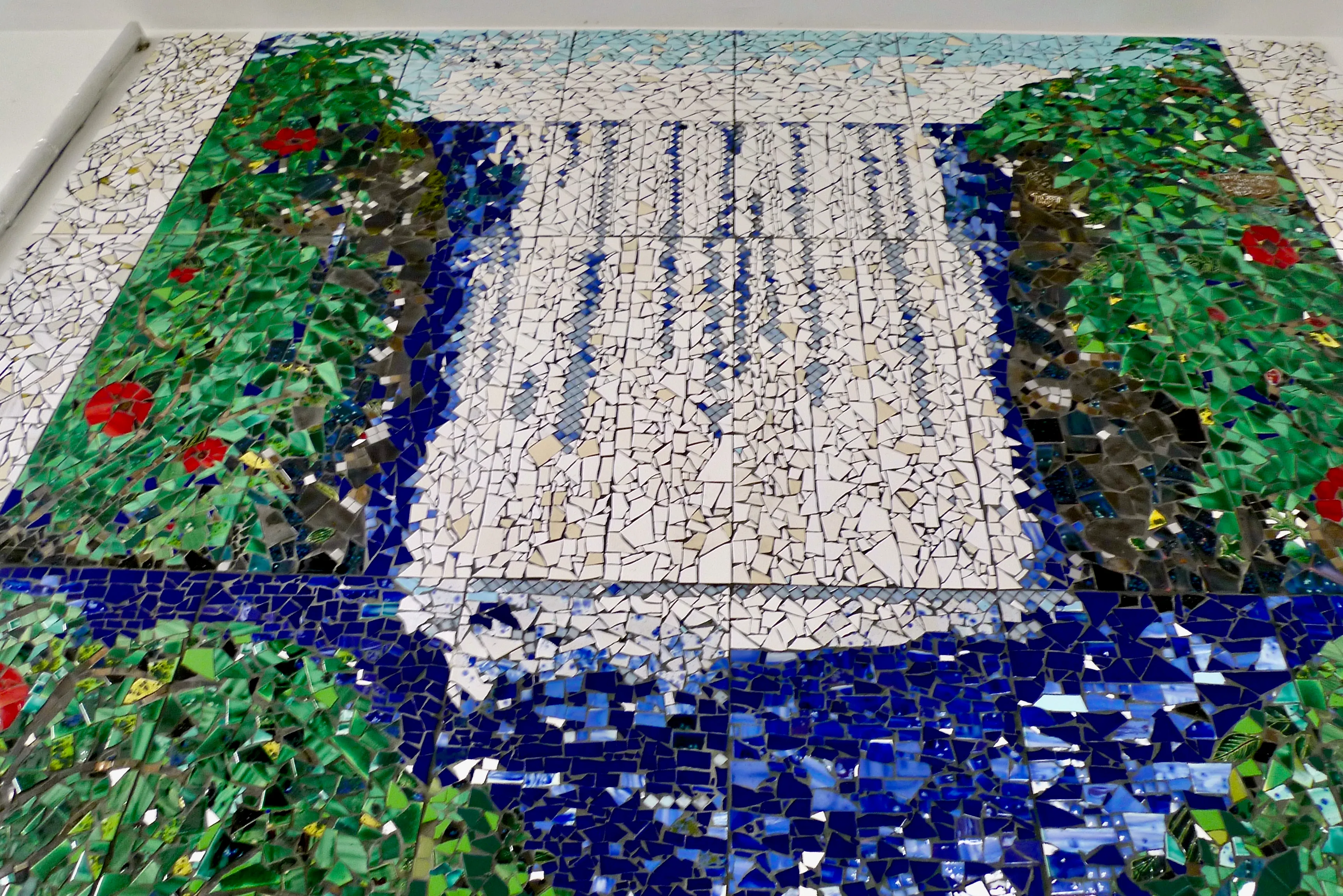 Mosaik mit einem Wasserfall, der von grünem Laub mit roten Blüten umgeben ist.