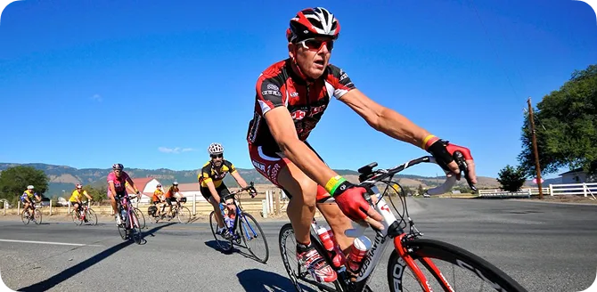Group of cyclists riding on a road with clear blue sky and hills in the background.