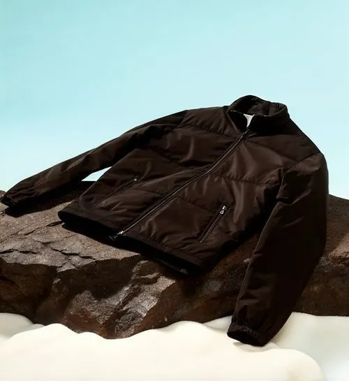Dark brown zip-up jacket with elastic cuffs displayed on a textured rock against a light blue background.