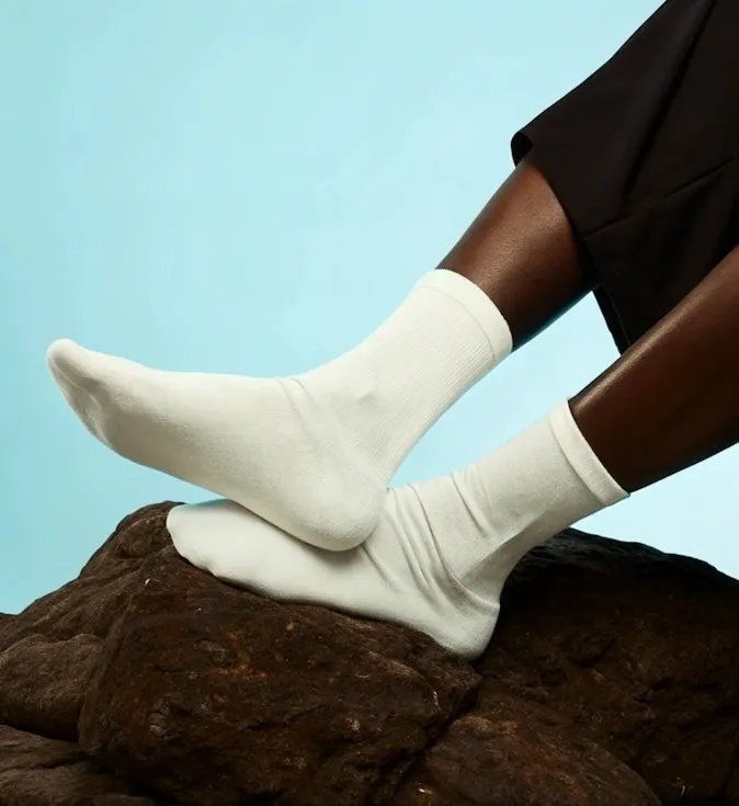 Close-up of dark-skinned legs wearing white socks resting on textured brown rocks against a light blue background.