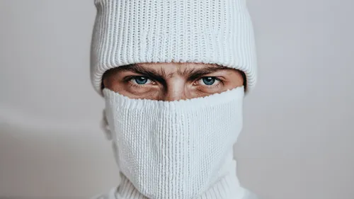 Close-up of a person with blue eyes wearing a white knit hat and a matching knit face covering.
