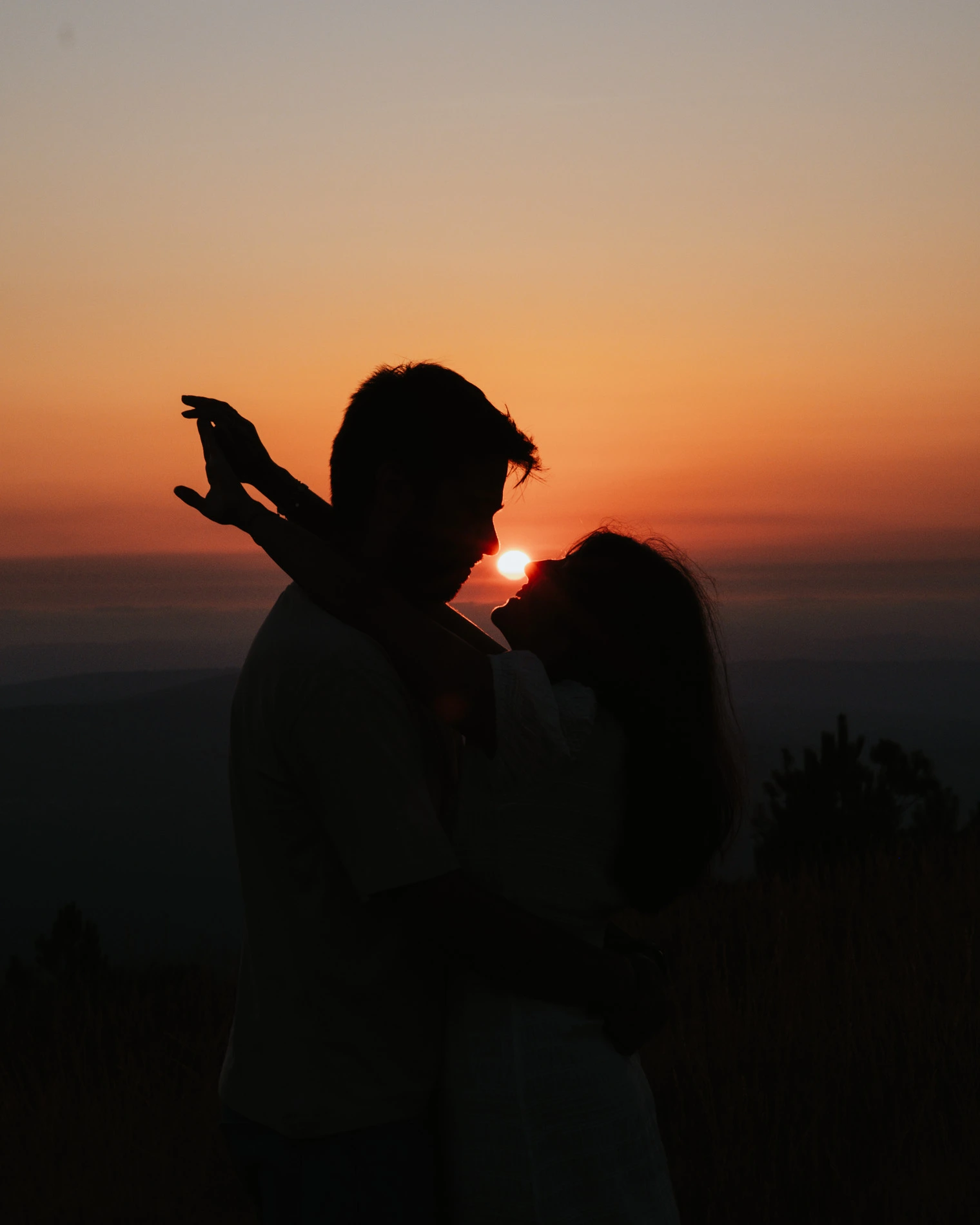 Silhouetted couple embracing and looking at each other against a sunset sky.