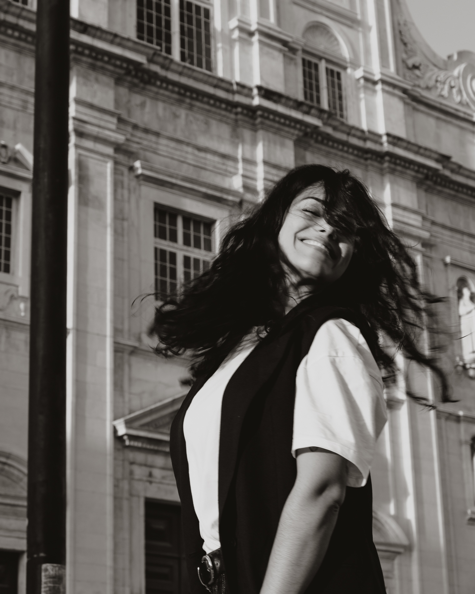 Smiling woman with long flowing hair standing outdoors in front of a historic building.