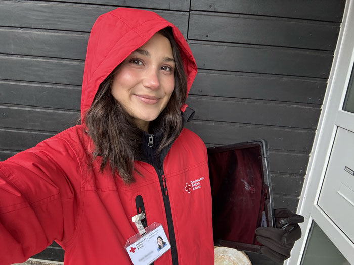 Selfie einer Fundraiserin die in einer Regenjacke des DRK und mit Tablet unter dem Arm vor einer Haustüre steht.