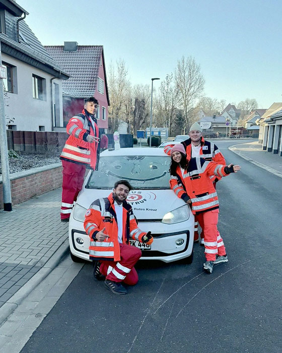 Vier Fundraiser posieren in winterfester Ausrüstung rund um ein Auto des DRK, auf dessen gefrorene Windschutzscheibe ein lächelndes Gesicht gemalt wurde.