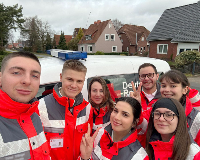 Eine Gruppe Fundraiser steht lachend vor einem Einsatzwagen des Deutschen Roten Kreuzes.