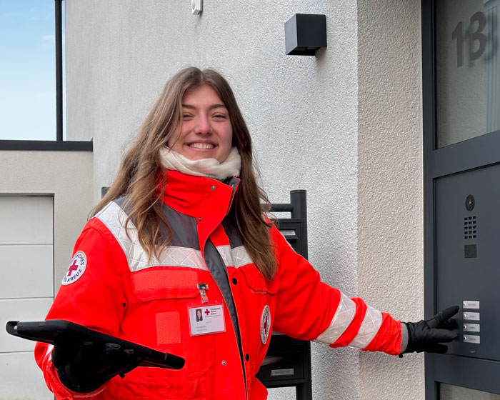 Eine junge Fundraiserin in Ausrüstung des DRK steht lächelnd vor einer Haustüre und betätigt die Klingel. Trotz kalter Temperaturen ist sie gut gelaunt.