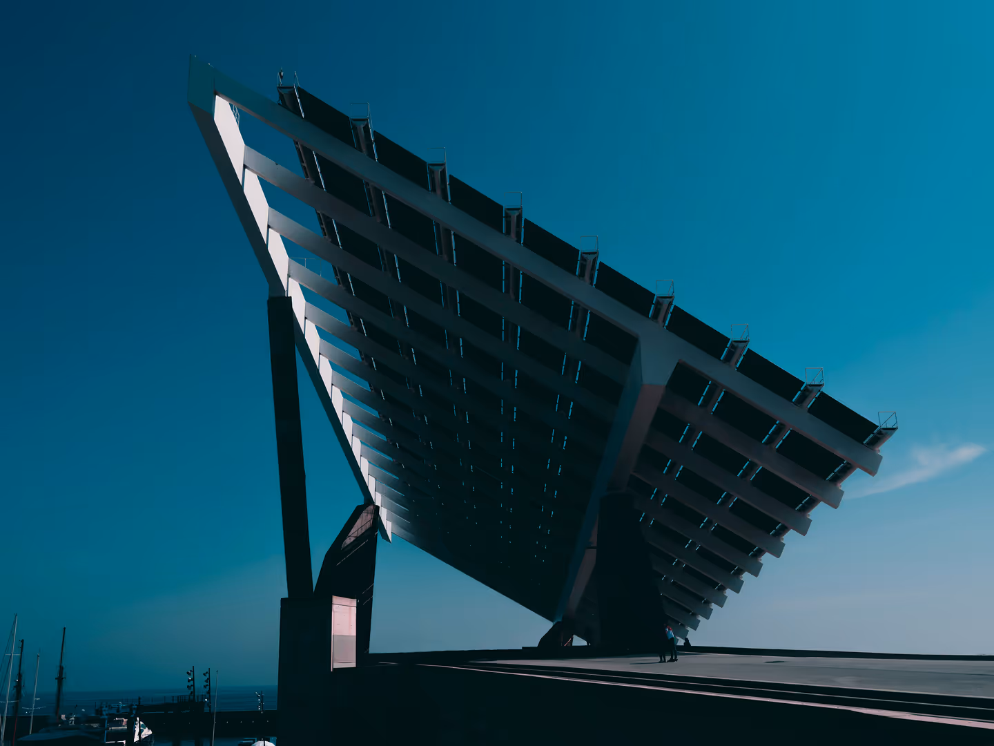Large angled solar panel structure with a clear blue sky background and a small person standing beneath it.