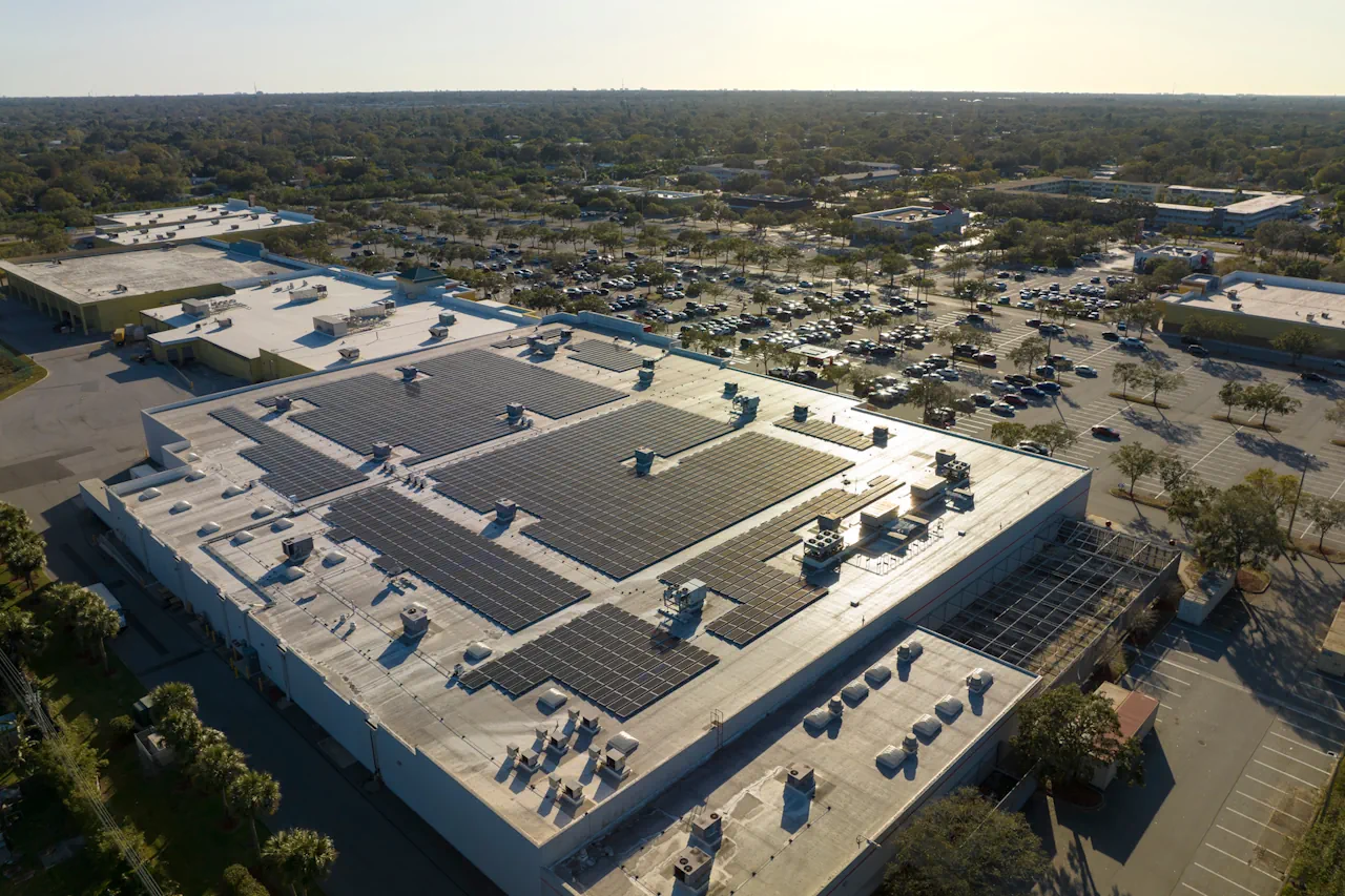 Aerial view of a large commercial building with multiple solar panel arrays on the roof and a parking lot in the background.
