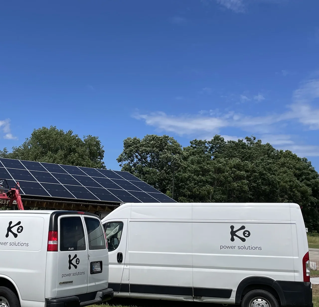 Two white vans with K2 Power Solutions logo parked near a solar panel array under a blue sky.