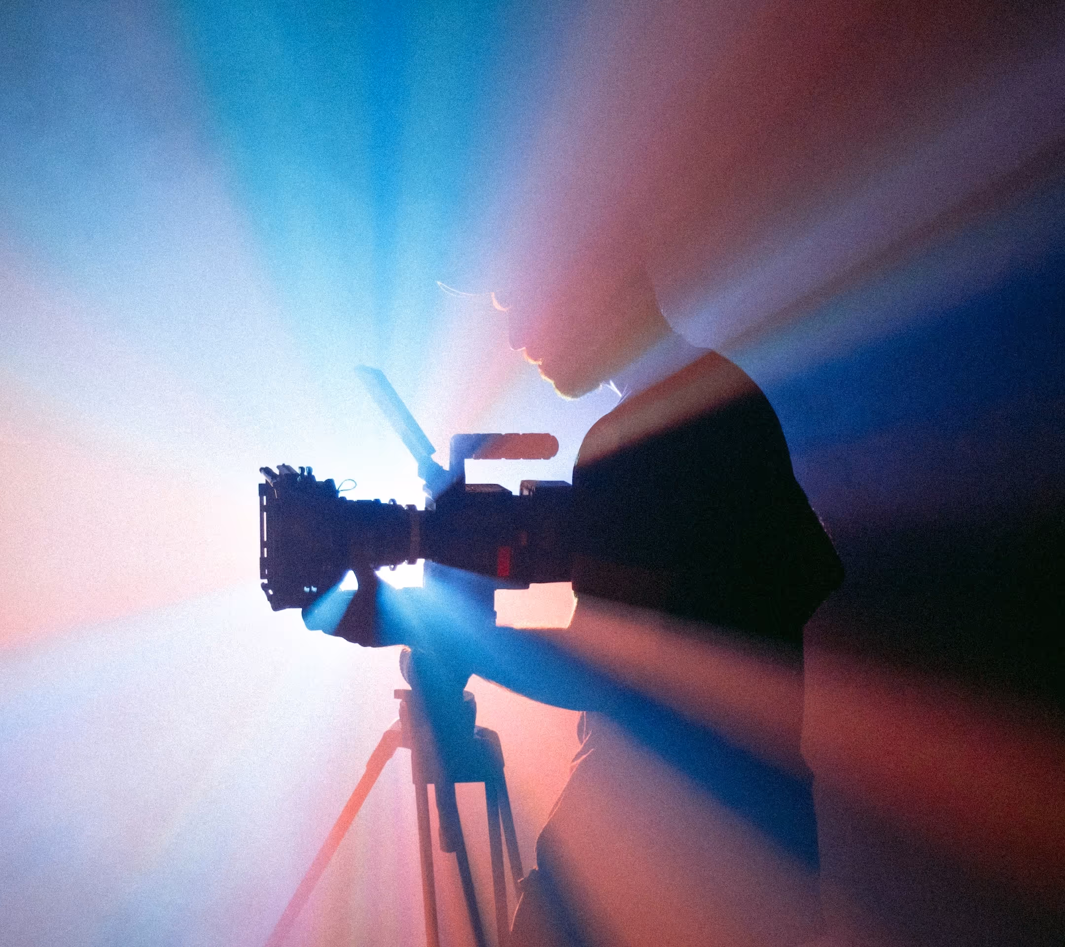 A videographer stood with their camera, backlit in a hazy room.