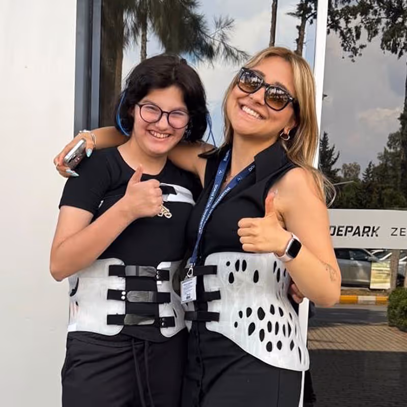 İki kadın, beyaz ortopedik korse takmış, elleriyle başparmak yukarı işareti yaparak gülümsüyor.