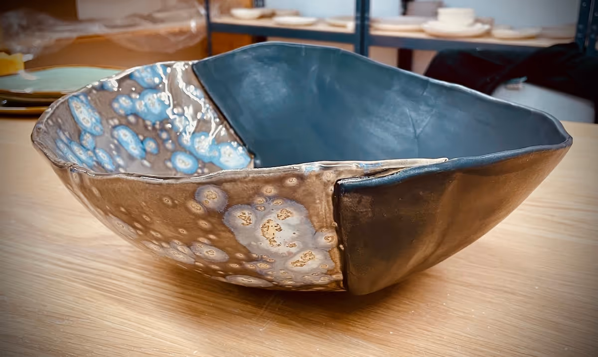 Rectangular ceramic bowl with a textured exterior featuring blue and tan glazing and a matte dark blue interior on a wooden table.