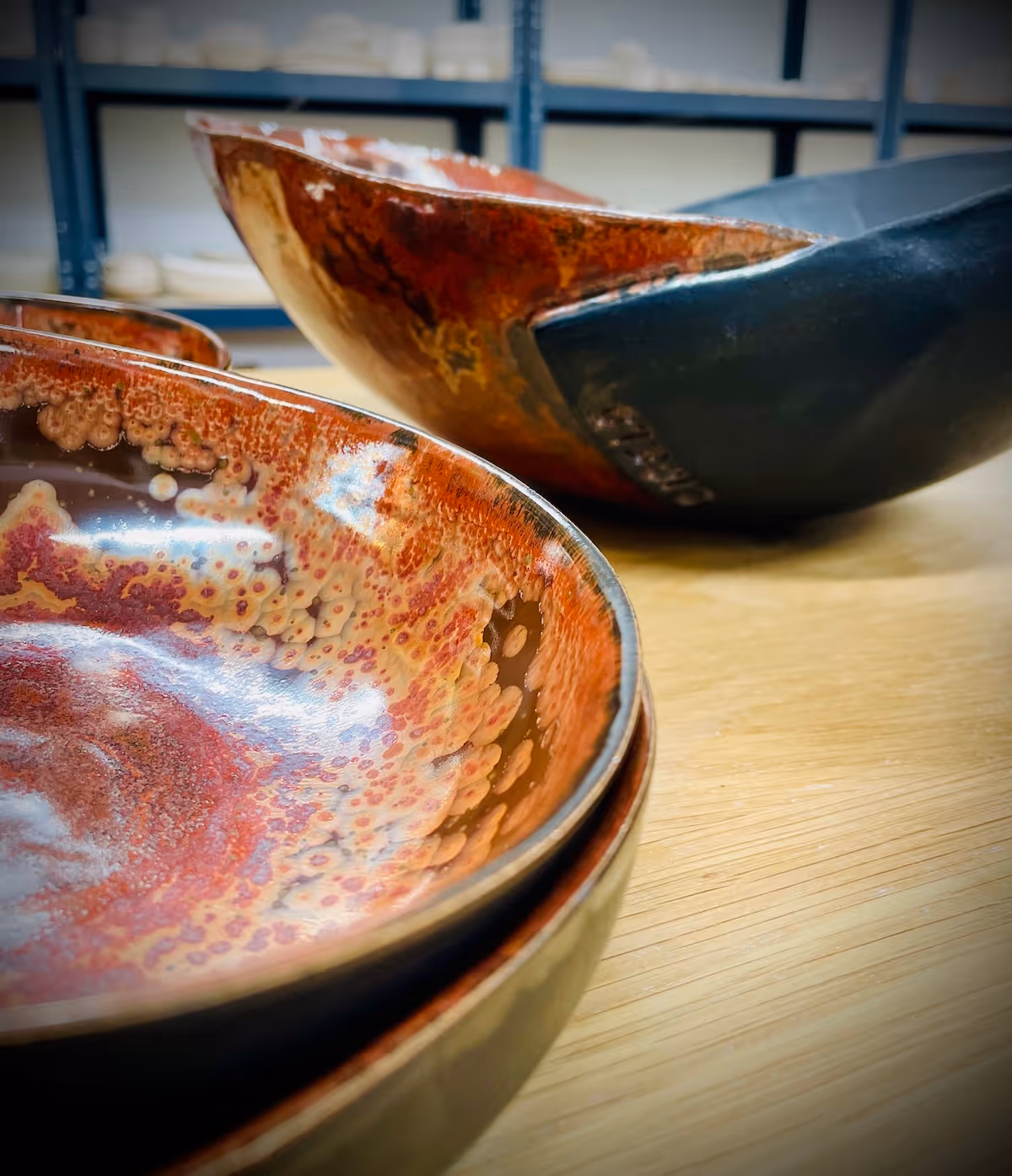 Close-up of two ceramic bowls with reddish-orange and yellow glaze patterns on a wooden surface.