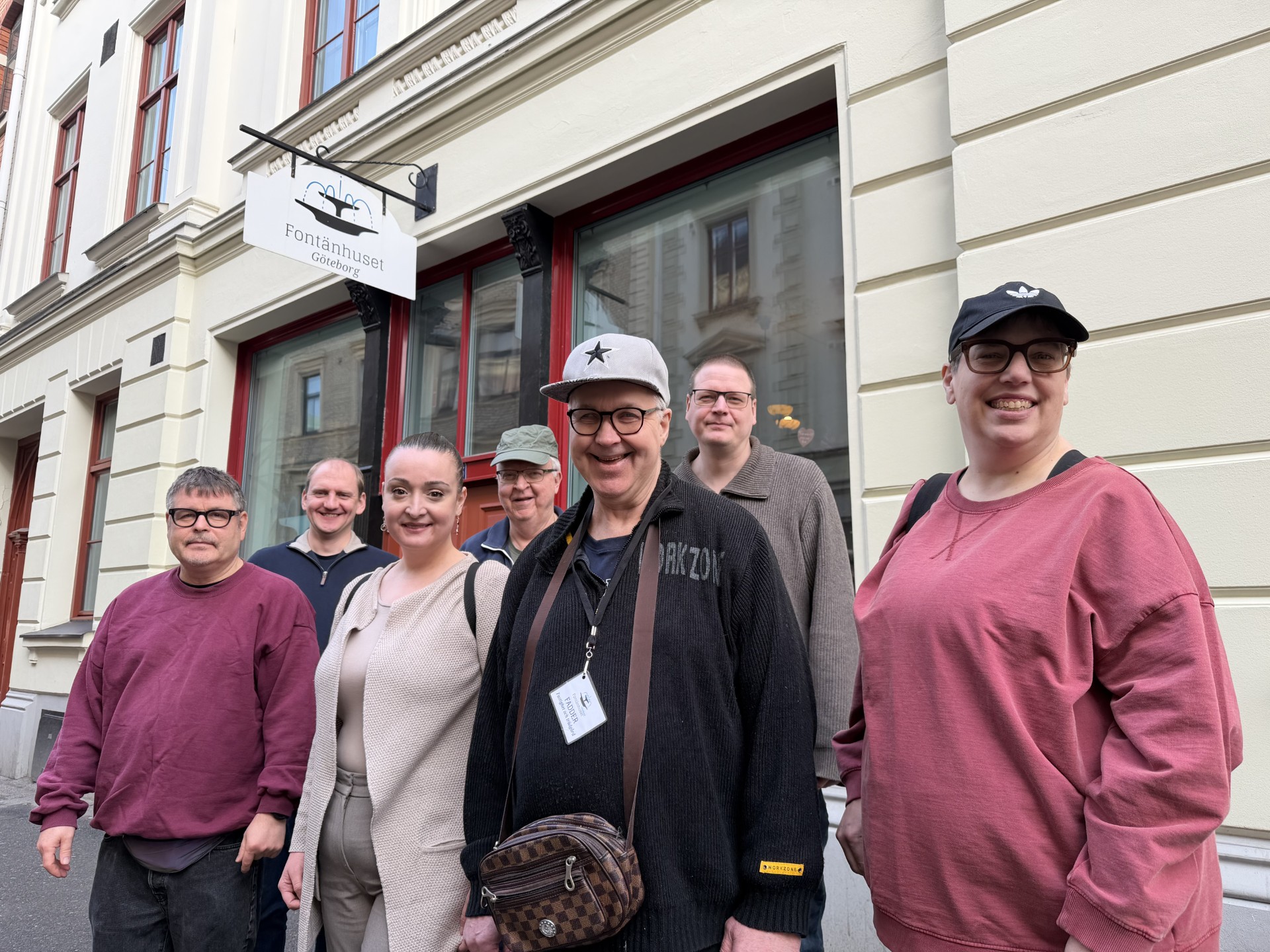 En grupp på sju personer står framför Fontänhuset Göteborgs byggnad och ler mot kameran.