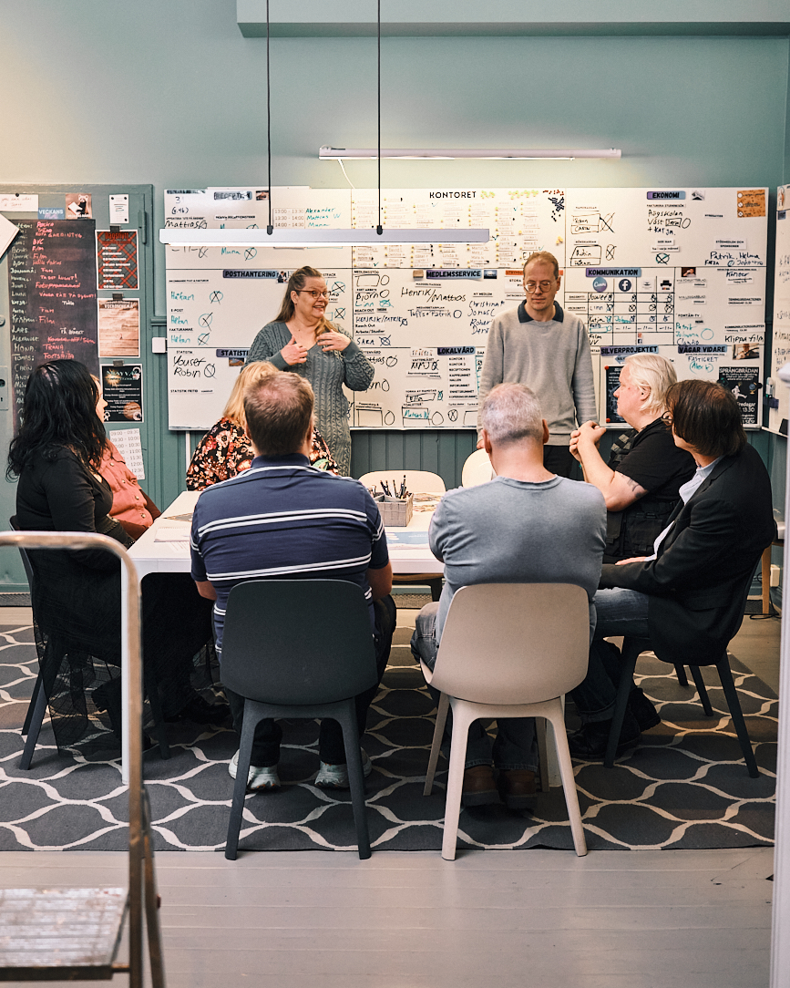 Grupp av sju personer i ett mötesrum med whiteboards fyllda med anteckningar i bakgrunden.