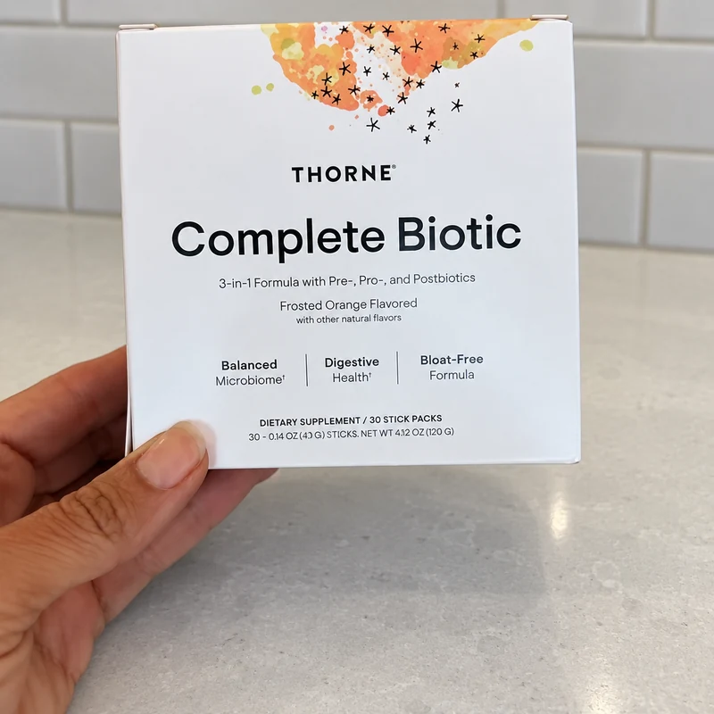 Hand holding a Thorne Complete Biotic box over a light quartz kitchen counter