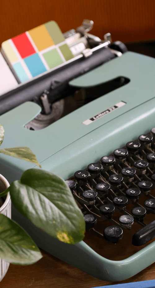 A mint-green typewriter beside a leafy plant