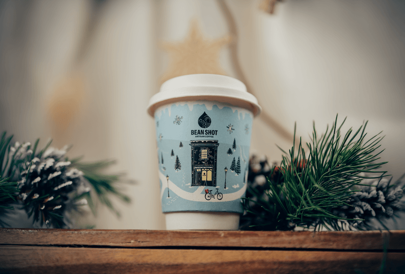 Beanshot illustrated takeaway coffee cup photographed with winter foliage.