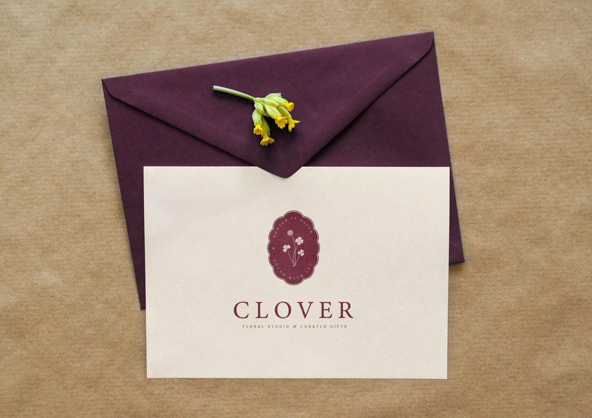 Clover floral studio logo on a cream card beside a burgundy envelope and yellow flowers.