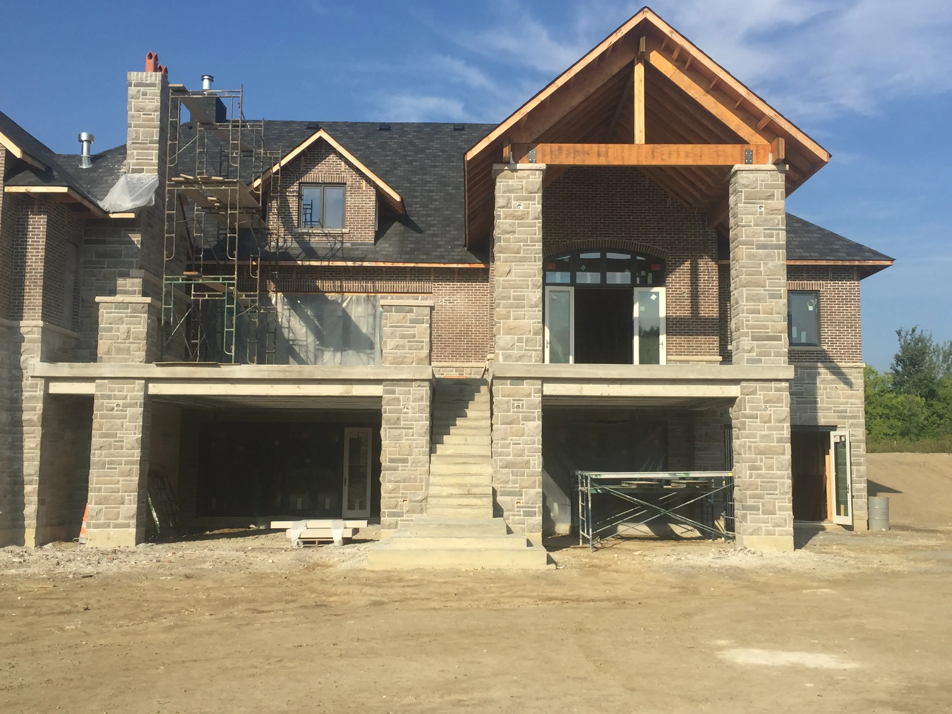 Stone and brick custom home under construction with completed concrete porch and stairs