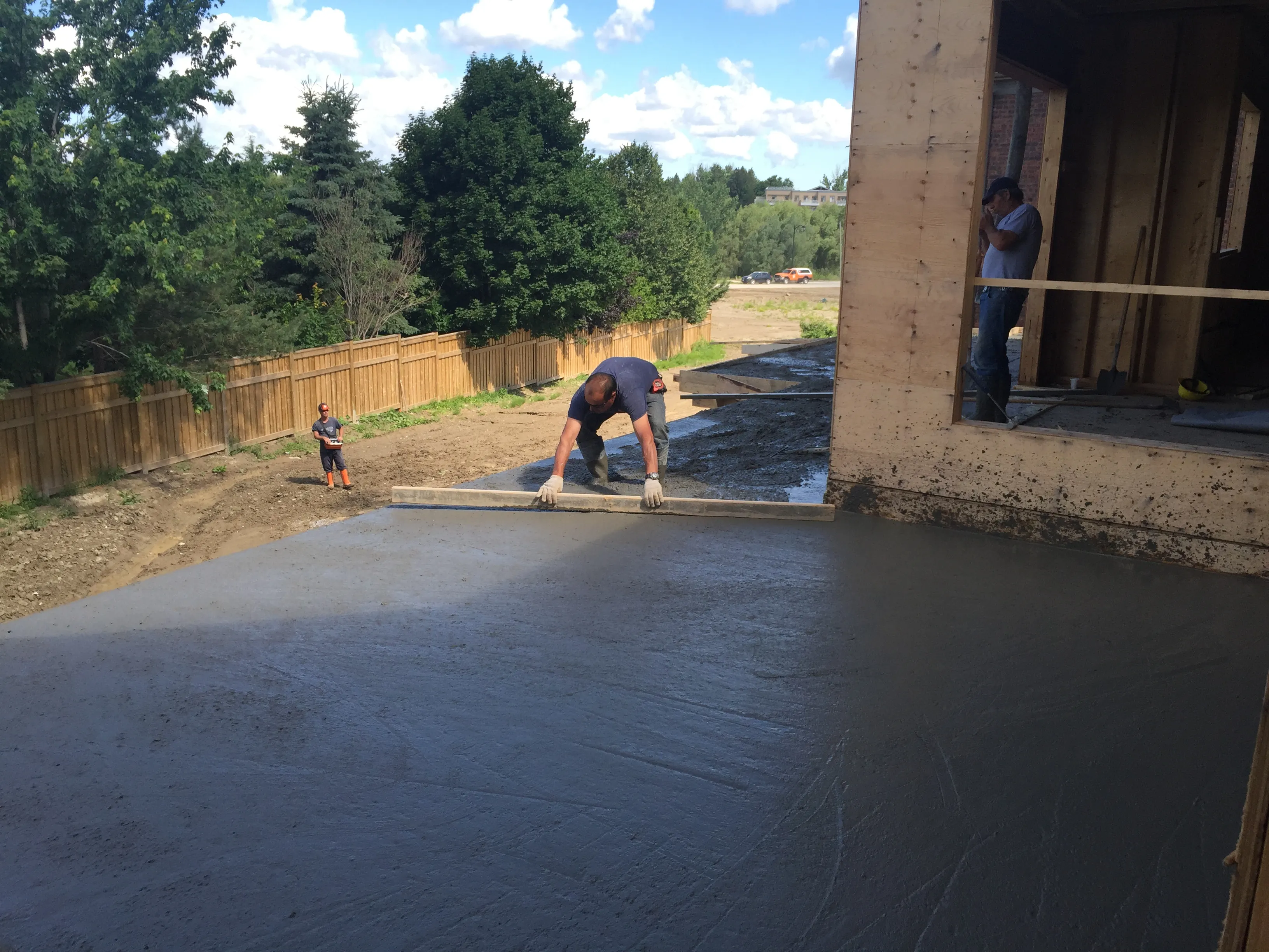 Worker screeding a freshly poured concrete slab on a residential lot