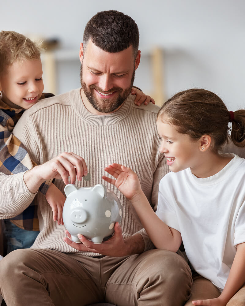 Father and two children smiling and putting coins into a piggy bank.