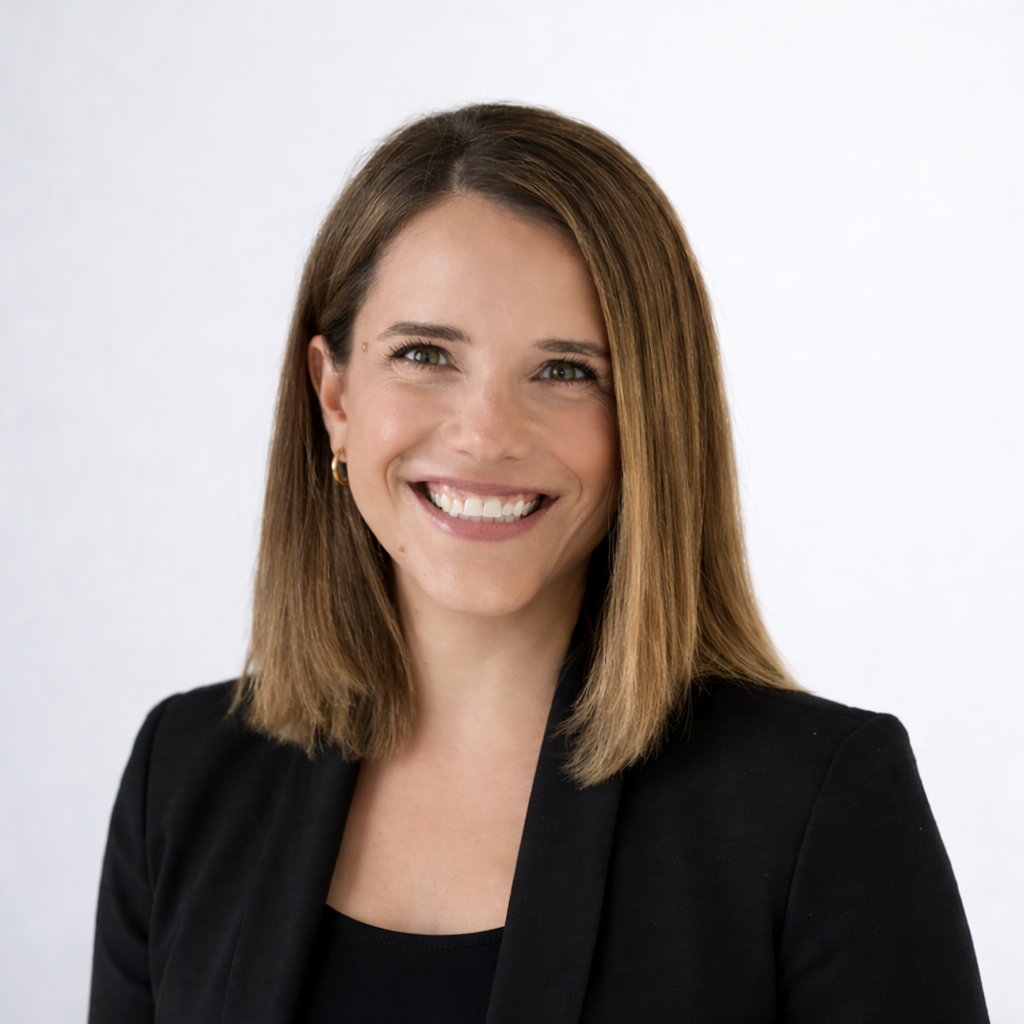 Smiling woman with shoulder-length straight brown hair wearing a black blazer against a light gray background.