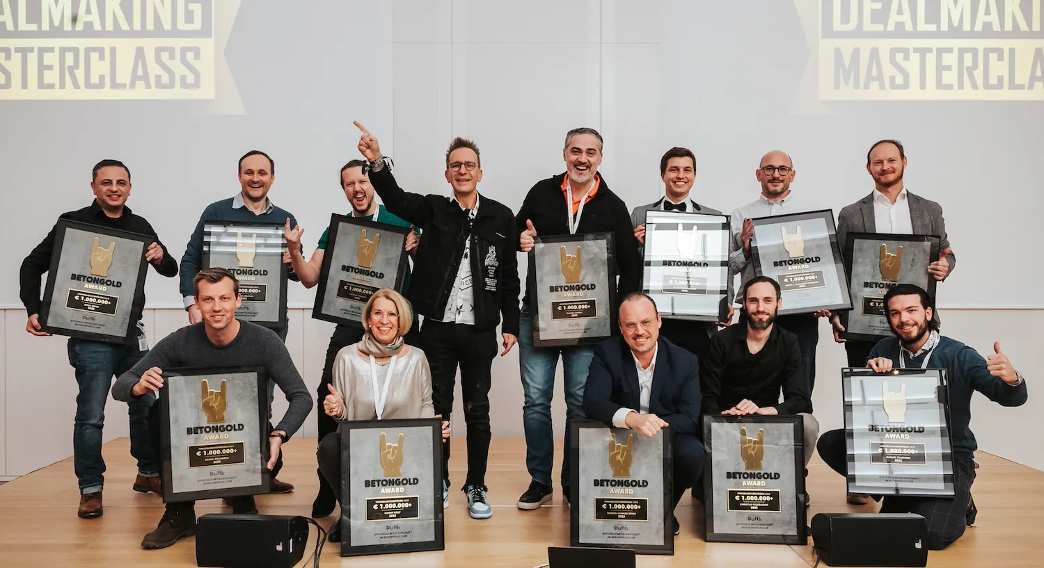 Gruppe von elf Personen auf einer Bühne hält große gerahmte BETONGOLD-Awards mit dem Betrag von über 1.000.000 Euro und zeigt Daumen hoch oder jubelt.