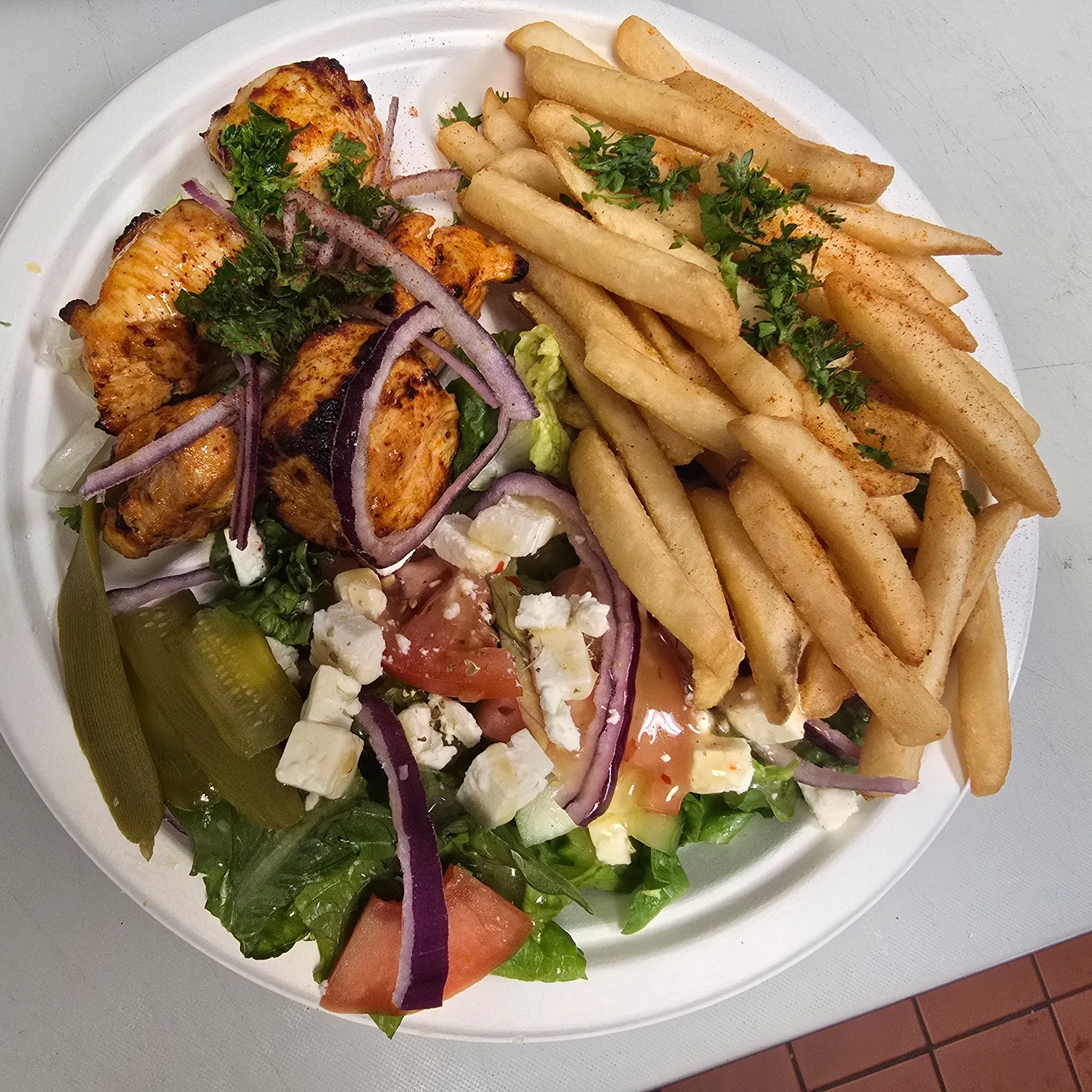 A plate of food with chicken, fries, tomatoes, onions, and lettuce.