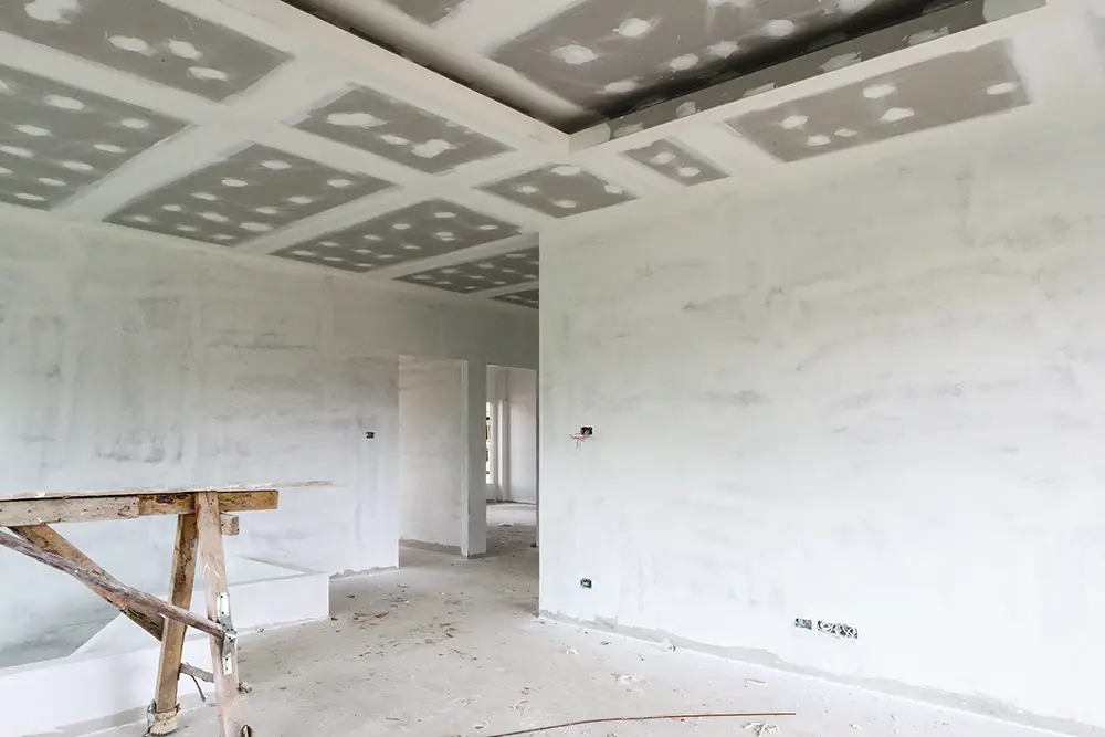 Room under construction with unfinished drywall ceiling and walls, and wooden scaffolding.
