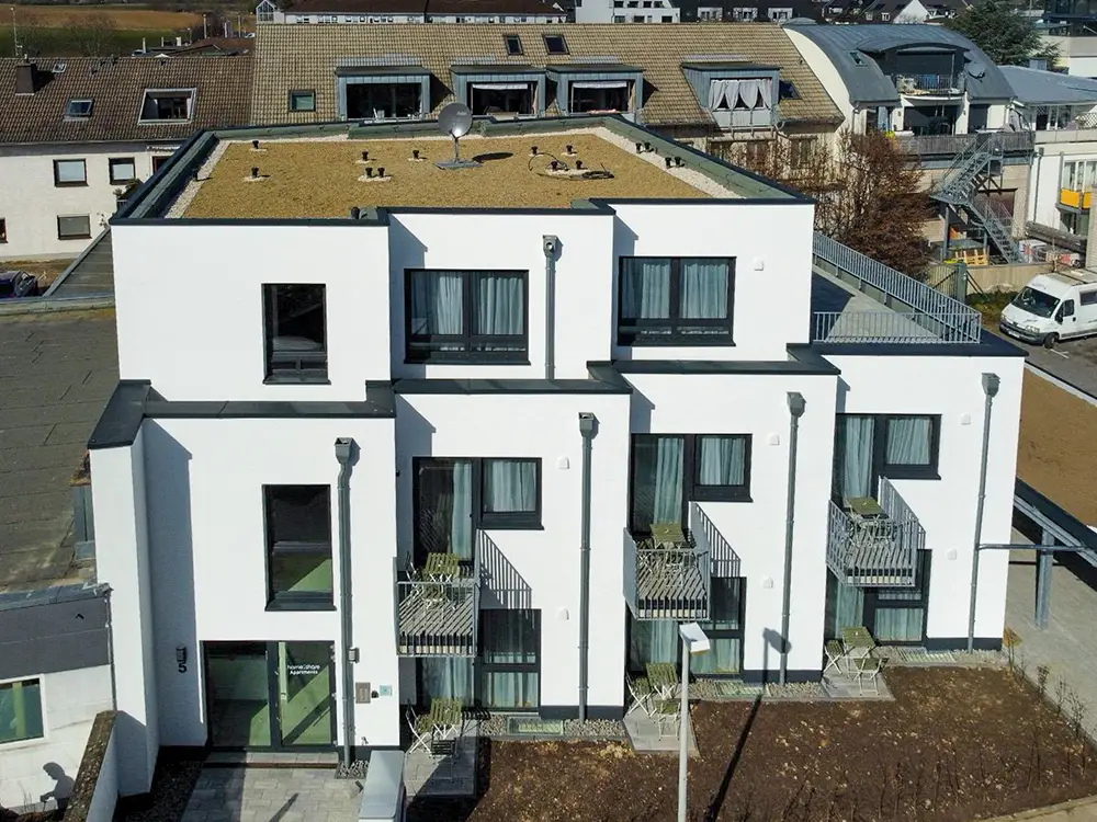 Modern white apartment building with small balconies, patio furniture, and a flat roof with satellite dish.