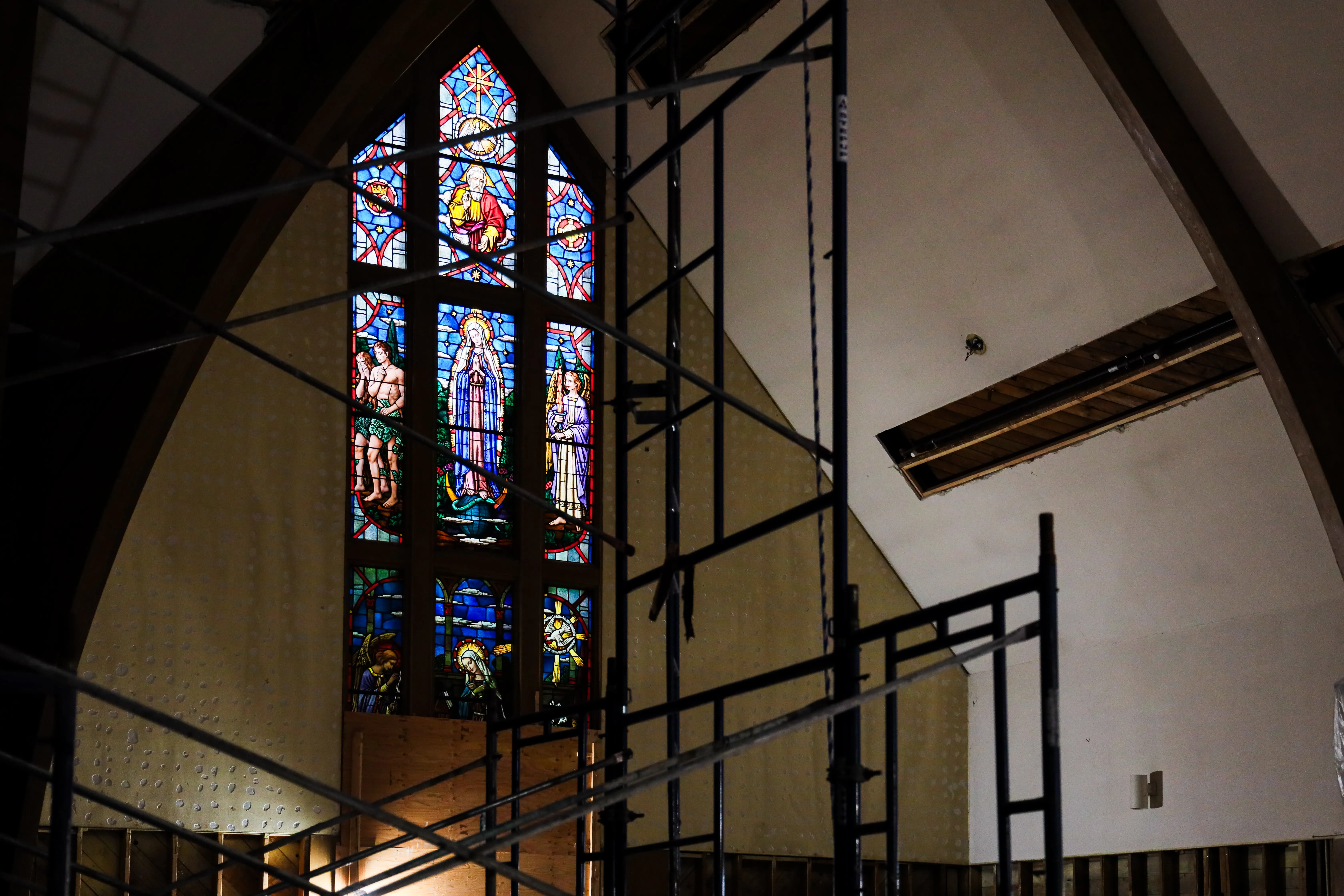 Interior of a church with wooden beams and pews filled with people facing a group of clergy at the altar in front of large windows.
