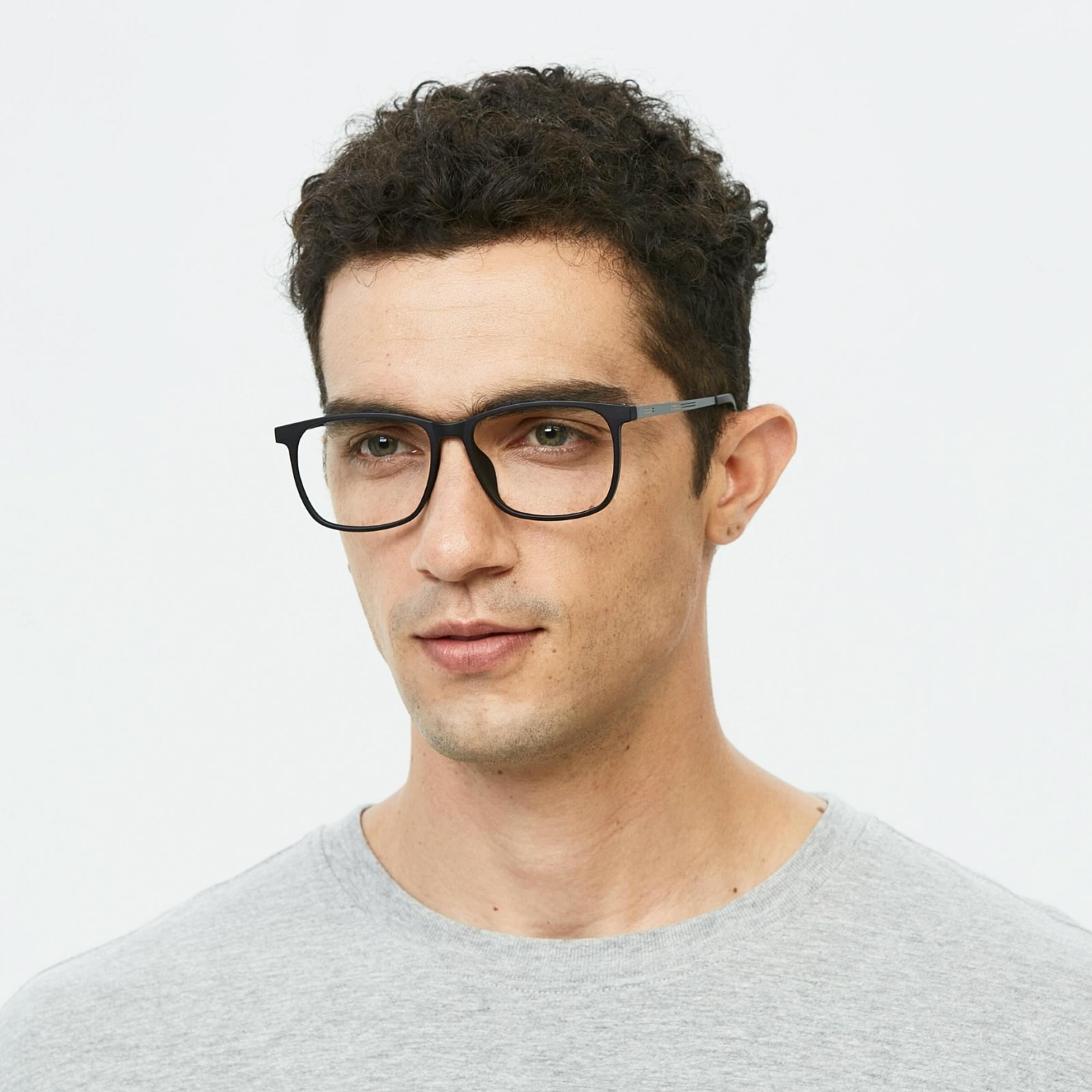 Close-up of a man with curly dark hair wearing black-framed glasses and a light gray shirt against a white background.