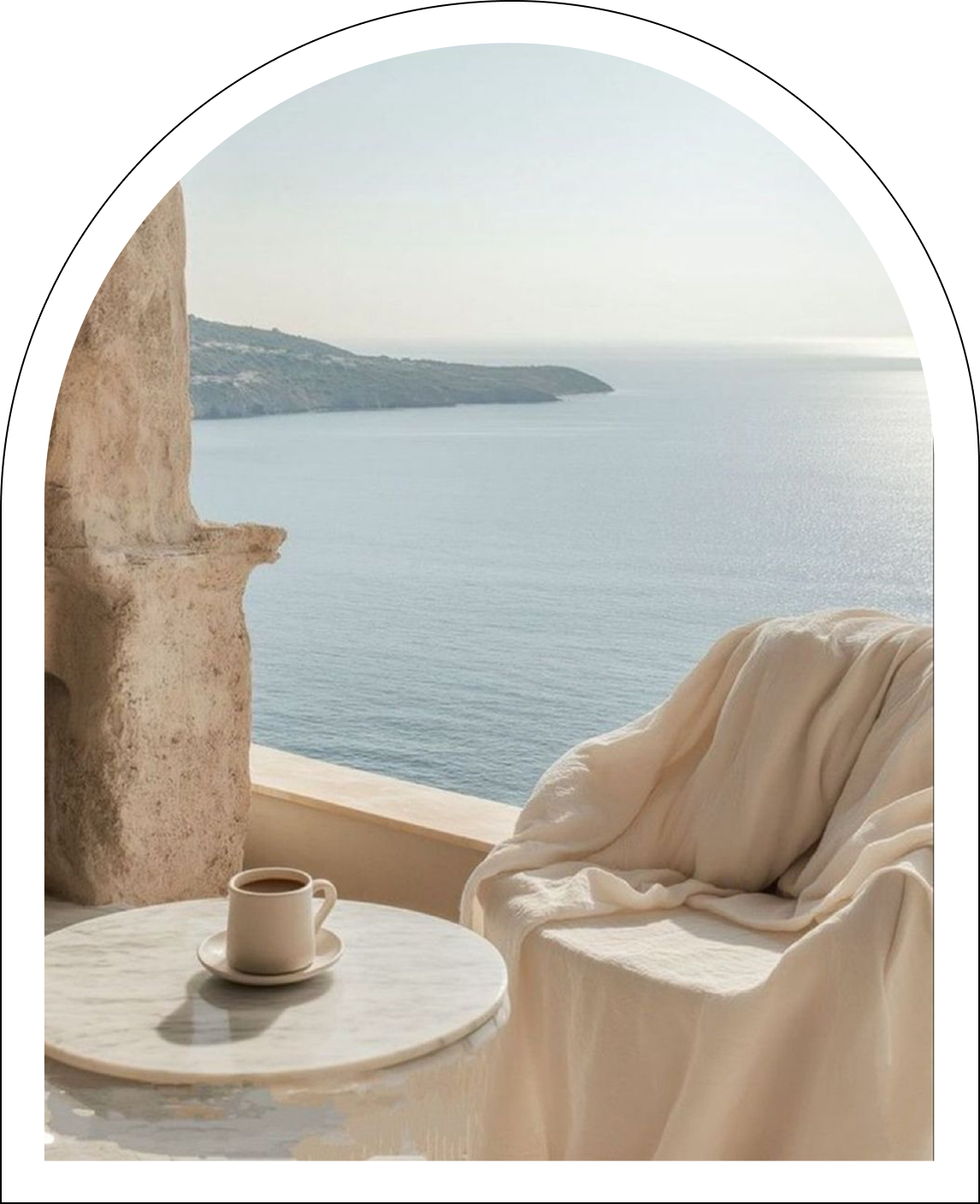Cozy chair draped with a light blanket beside a marble table with a cup, overlooking a calm sea and distant land under soft daylight.