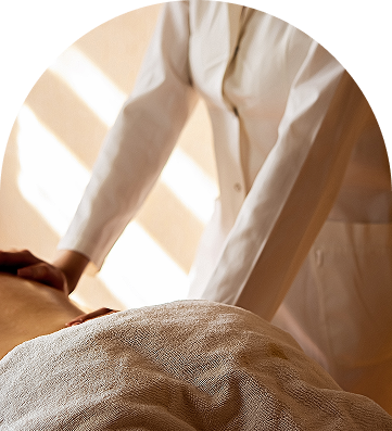 Person receiving a massage with a therapist's hands applying pressure on their back, covered by a towel.