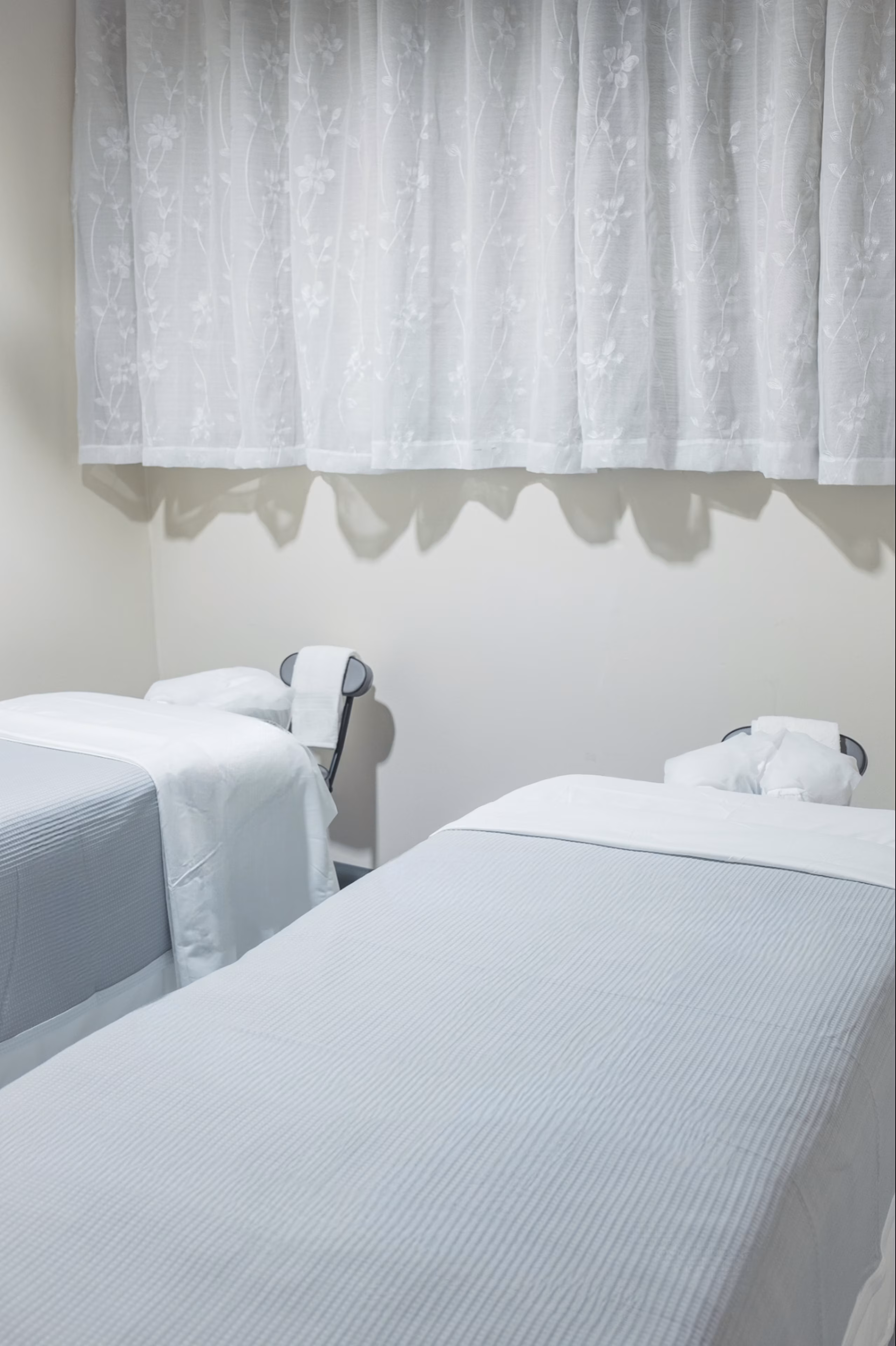 Two wooden lounge chairs with blankets beside a pool overlooking a serene sea and distant mountains.