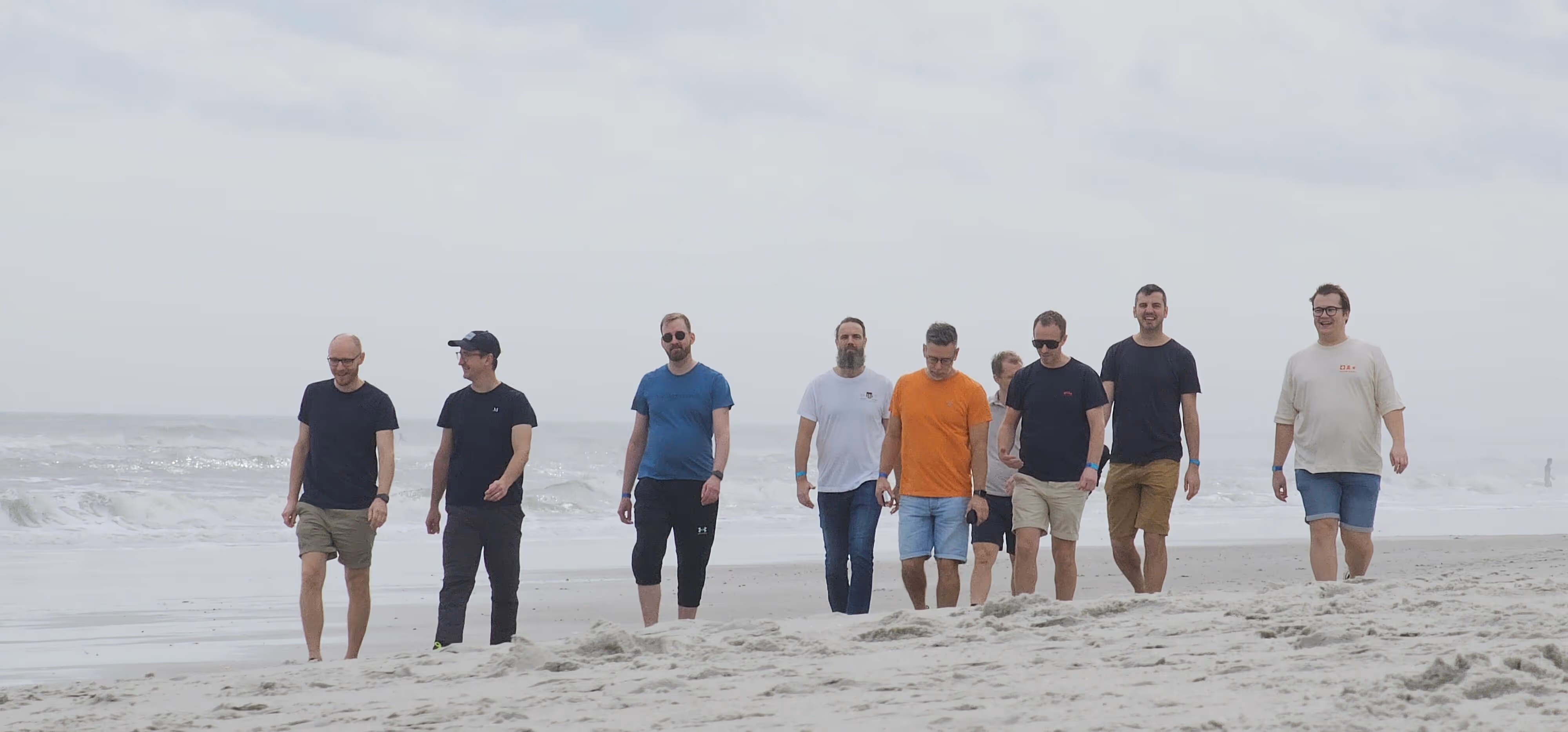 Group of men casually walking together on a cloudy beach near the ocean.