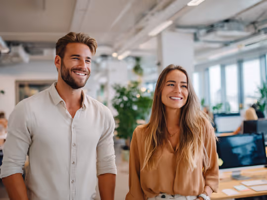 Smiling man and woman standing side by side in a modern office environment.